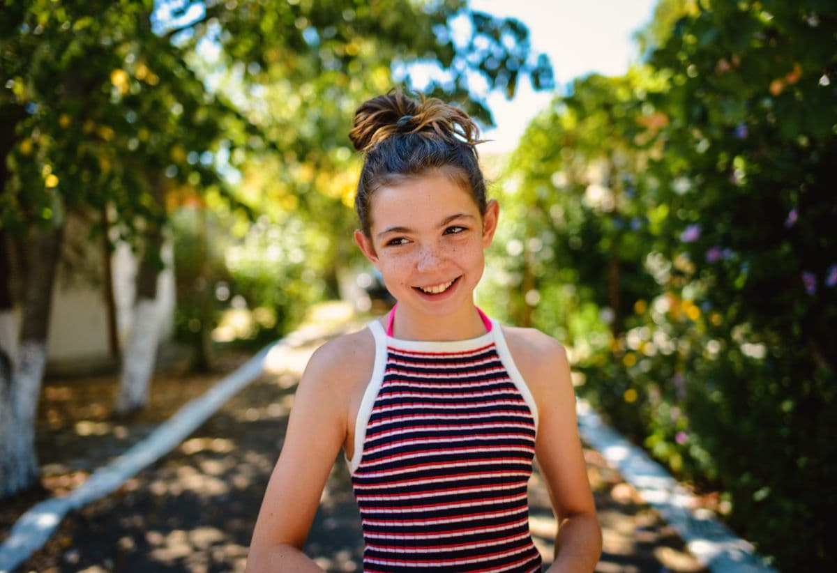 A young girl smiling brightly on a sunny garden path