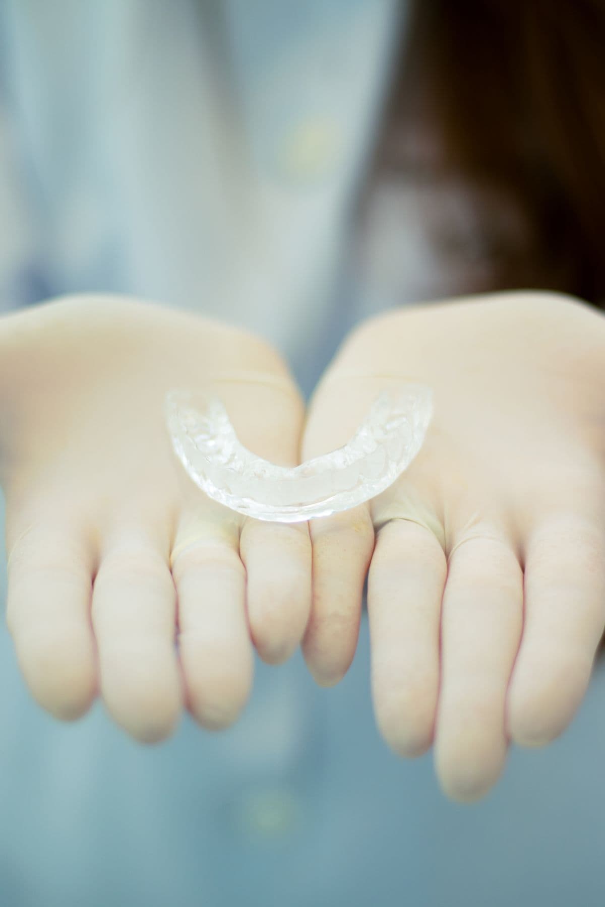 A clear aligner tray held in gloved hands